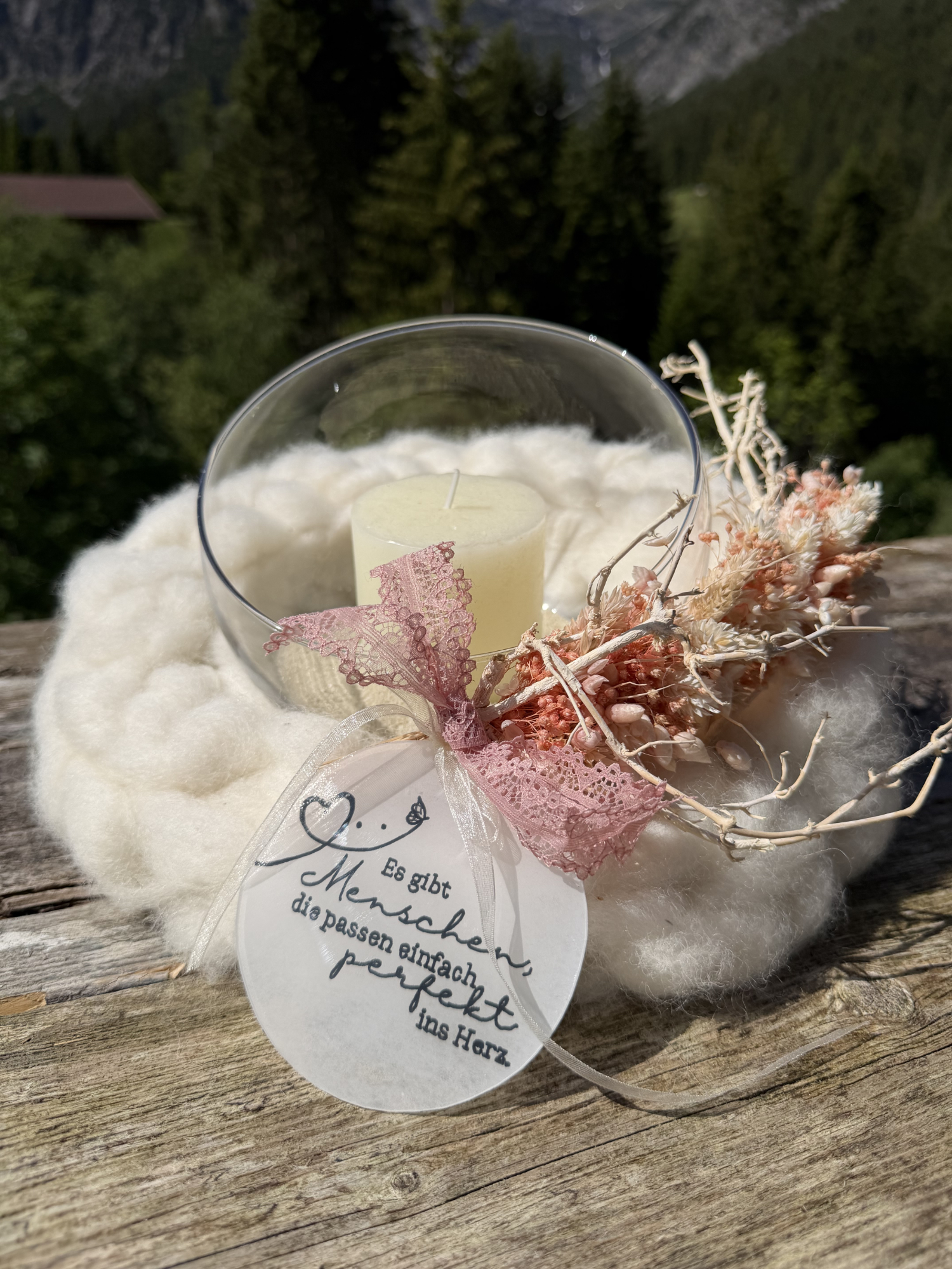 Windlicht in Schurwollnest mit Trockenblumen und Spitzenschleife, im Hintergrund Tiroler Alpen