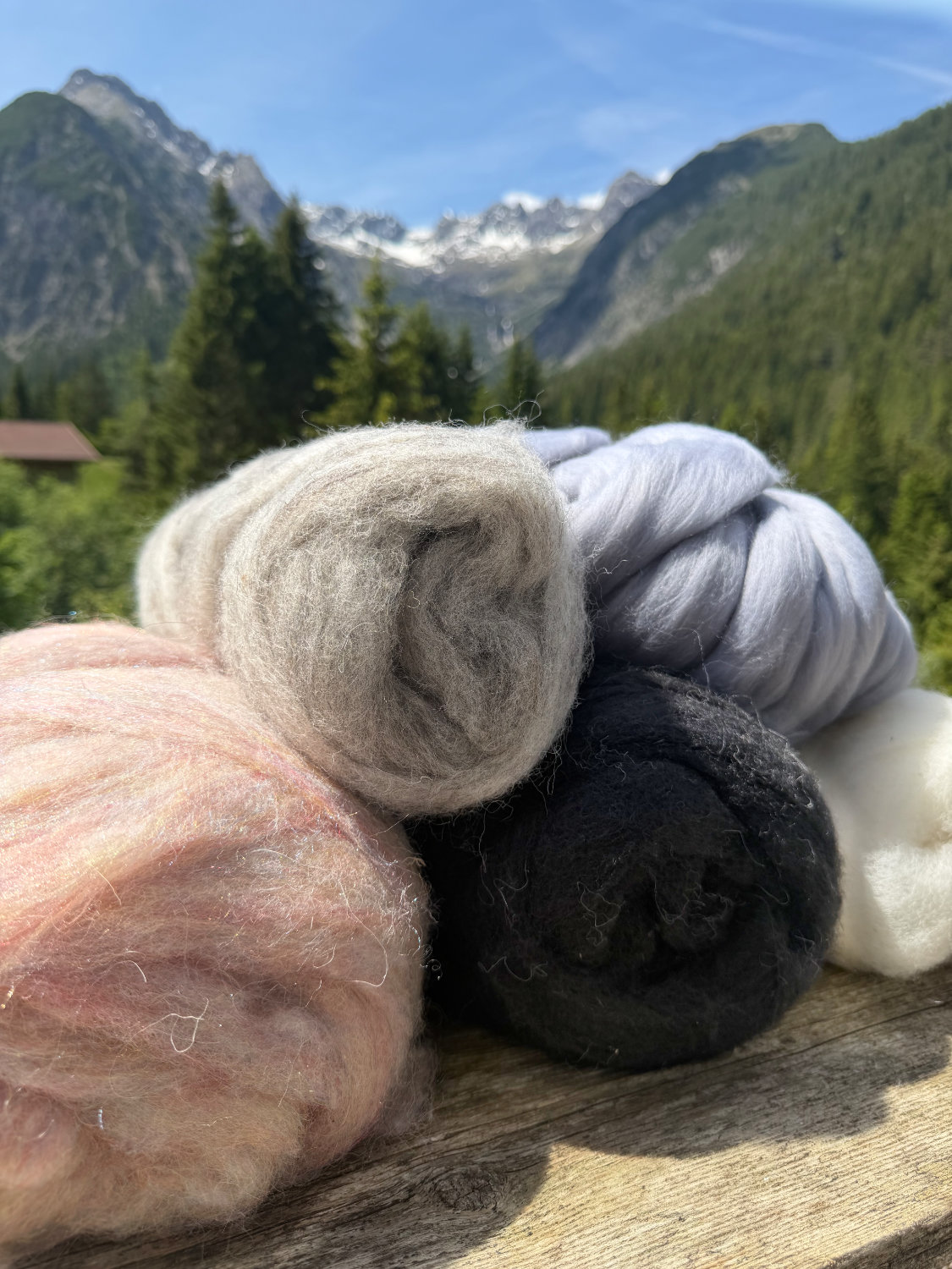 Wollknäuel in verschiedenen Farben – Rosa, Beige, Schwarz, Hellblau und Weiß – vor schneebedecktem Lechtaler Bergpanorama – Naturmaterialien NaturTraum Lechtal
