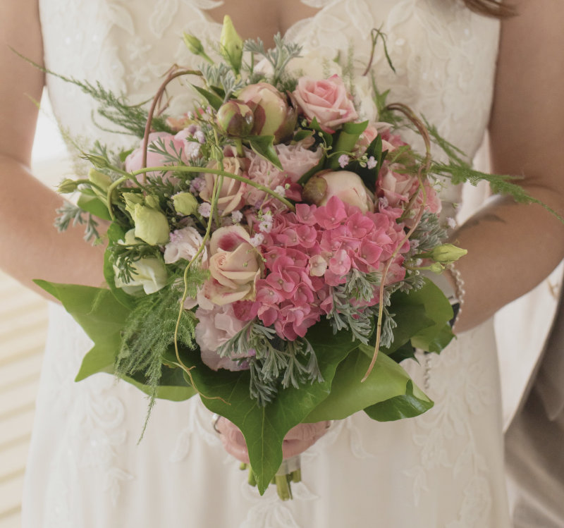 Braut hält Brautstrauß mit rosa Hortensien, Pfingstrosen und Rosen im Spitzenkleid – Hochzeitsfloristik von NaturTraum