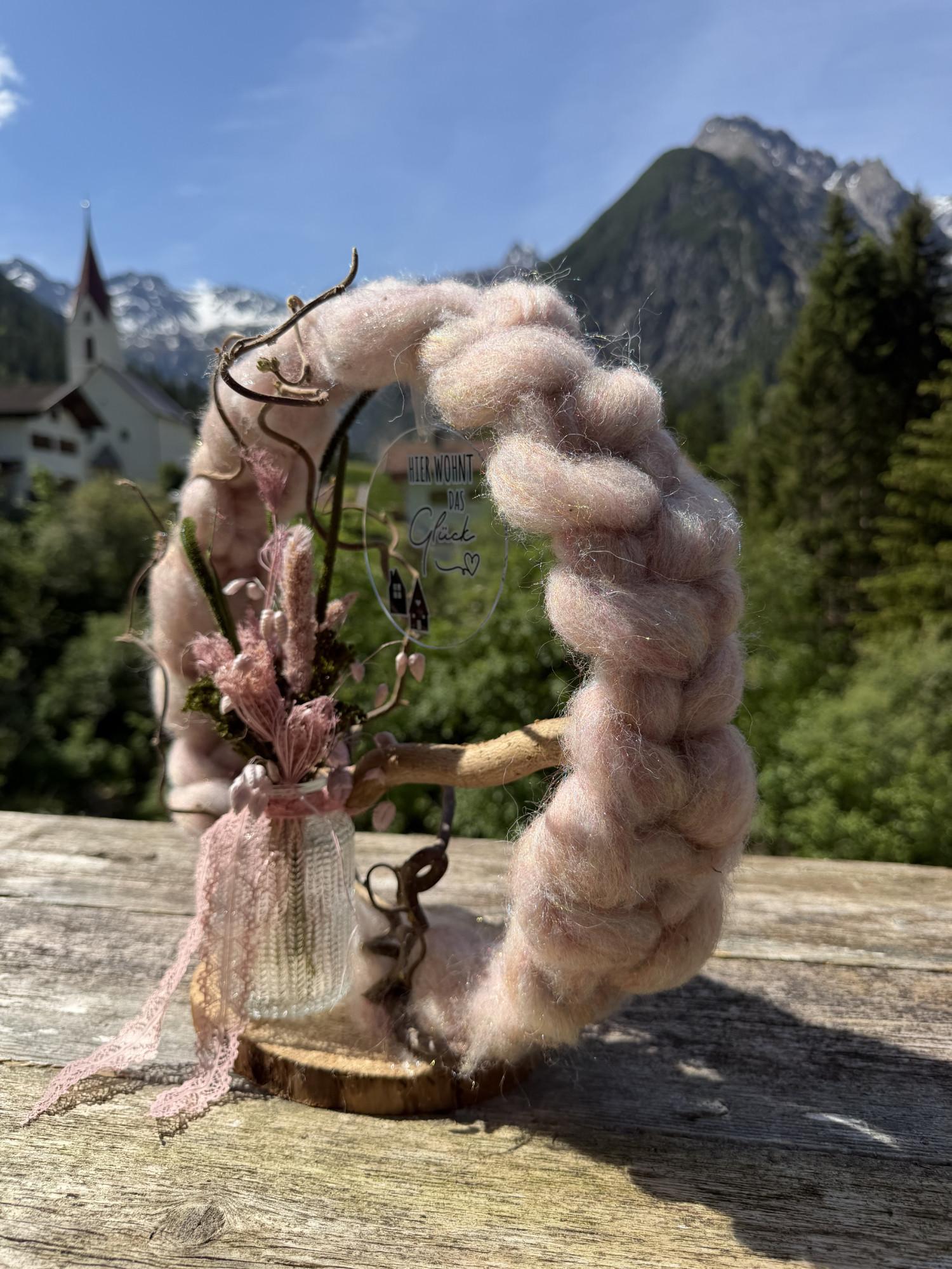 Nahaufnahme des Dekorings „Rosalie" mit Spitzenband, Moos und Federgras-Detail vor Tiroler Alpenkulisse