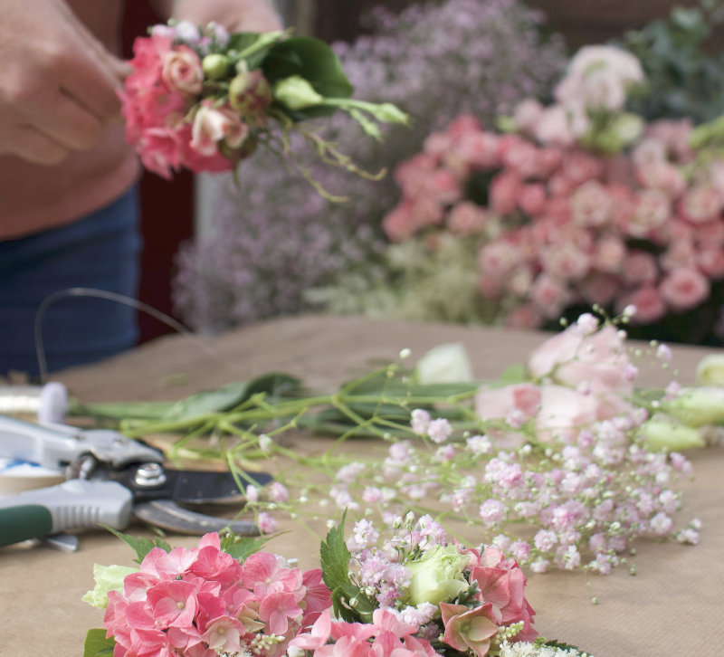 Floristin bindet Blumengesteck aus rosa Hortensien und Schleierkraut an einem Arbeitsplatz mit Blumenschere – Floristik NaturTraum Lechtal